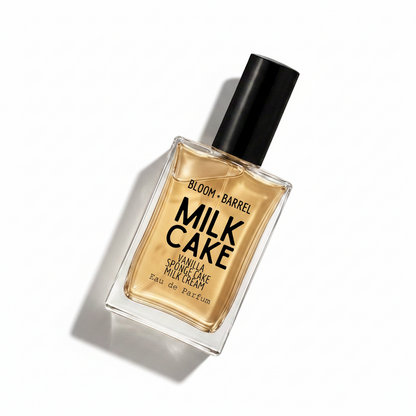 Bloom Barrel Milk Cake Vanilla Sponge Cake Milk Cream Eau de Parfum in a clear rectangular glass bottle with a black cap, showing the golden-amber fragrance liquid inside, on a solid white background.