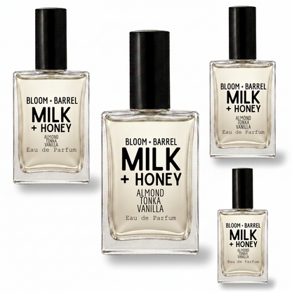 Four clear glass perfume bottles with black caps arranged on a white background. The center bottle is largest, with three smaller identical bottles around it.