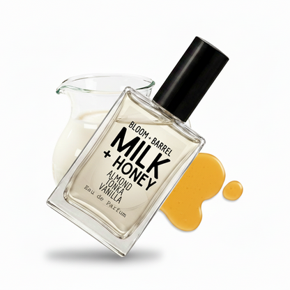 A rectangular glass perfume bottle labeled 'BLOOM + BARREL MILK + HONEY' with a black cap, shown on a white background with a glass pitcher of milk and honey-colored syrup drips behind it.