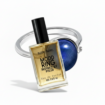 Bloom + Barrel Mood Ring Inspired By PHLR Eau de Parfum bottle in front of a silver mood ring with a blue stone, on a white background.