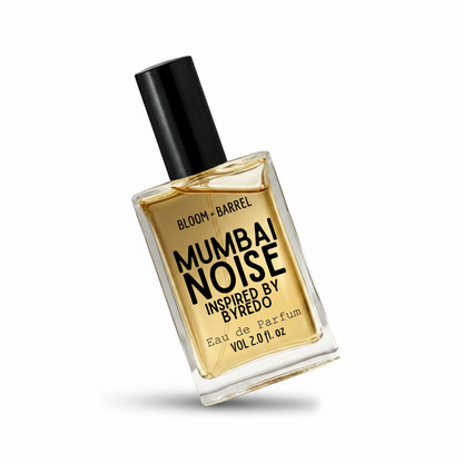 A rectangular glass perfume bottle filled with golden amber liquid, featuring a black cylindrical cap and a clear label with bold black text reading 'MUMBAI NOISE' and smaller text 'BLOOM + BARREL' and 'INSPIRED BY BYREDO'.