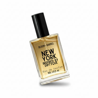 A rectangular glass bottle of Bloom + Barrel New York Inspired By Diptyque Eau de Parfum with a black cap, filled with golden-yellow liquid, on a plain white background.