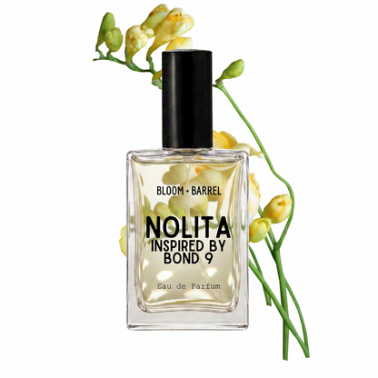A rectangular glass perfume bottle with a black cap and a cream-colored label reading 'BLOOM • BARREL NOLITA INSPIRED BY BOND 9 Eau de Parfum', styled with yellow flower buds on a white background.