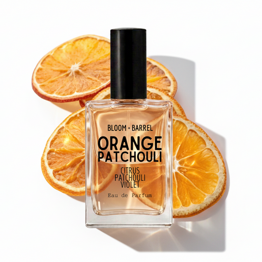 A bottle of Bloom + Barrel Orange Patchouli Eau de Parfum centered in front of dried orange slices on a white background.