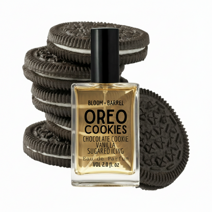 A bottle of Bloom + Barrel Oreo Cookies Eau de Parfum in a square glass bottle with a black cap, set against a background of stacked and leaning Oreo cookies. The liquid inside the bottle is a warm golden-amber color.