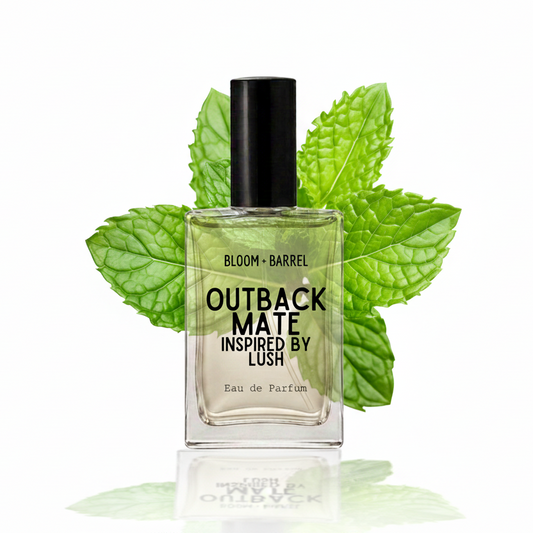 A clear glass perfume bottle with a black cap, labeled 'BLOOM • BARREL OUTBACK MATE INSPIRED BY LUSH', centered against a white background with green mint leaves behind it.