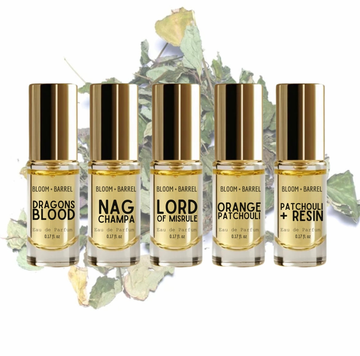 Five Bloom + Barrel perfume bottles arranged in a row on a white background with dried botanical leaves behind them. The bottles contain pale golden liquid and have shiny metallic gold caps.