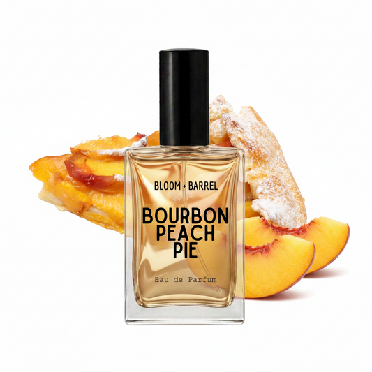 A rectangular glass perfume bottle labeled 'BLOOM • BARREL BOURBON PEACH PIE' with a black cap, centered in front of peach pie slices on a white background.