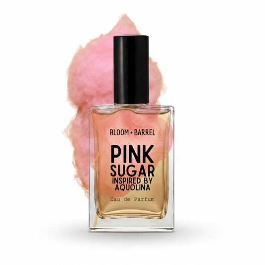 A bottle of Bloom Barrel Pink Sugar Eau de Parfum with a black cap and clear glass showing golden-amber liquid, set against a white background with a pink cotton candy graphic behind it.