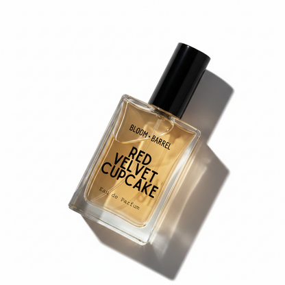 A rectangular glass perfume bottle with a black cap, filled with amber-colored liquid. The front label reads 'BLOOM • BARREL' and 'RED VELVET CUPCAKE Eau de Parfum' in black text, set against a plain white background.