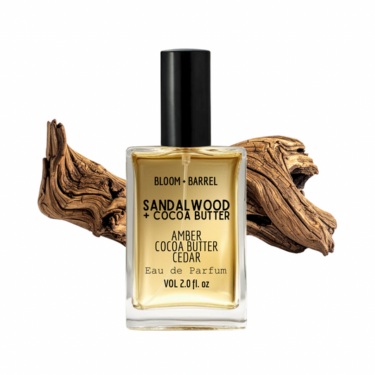 Perfume bottle labeled 'Sandalwood + Cocoa Butter' with decorative wood piece on a white background