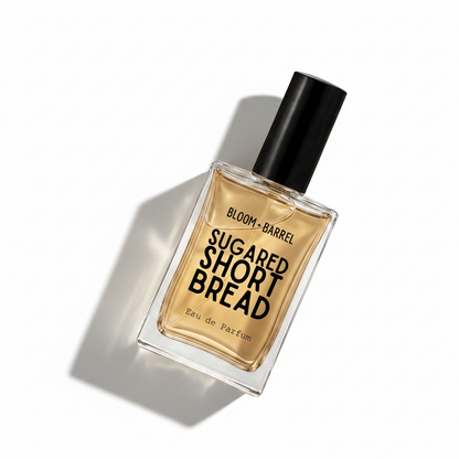 A rectangular glass perfume bottle filled with amber-colored fragrance liquid, featuring a black cylindrical cap and bold black text on the front reading 'BLOOM • BARREL' and 'SUGARED SHORT BREAD', with 'Eau de Parfum' near the bottom, set against a plain white background.