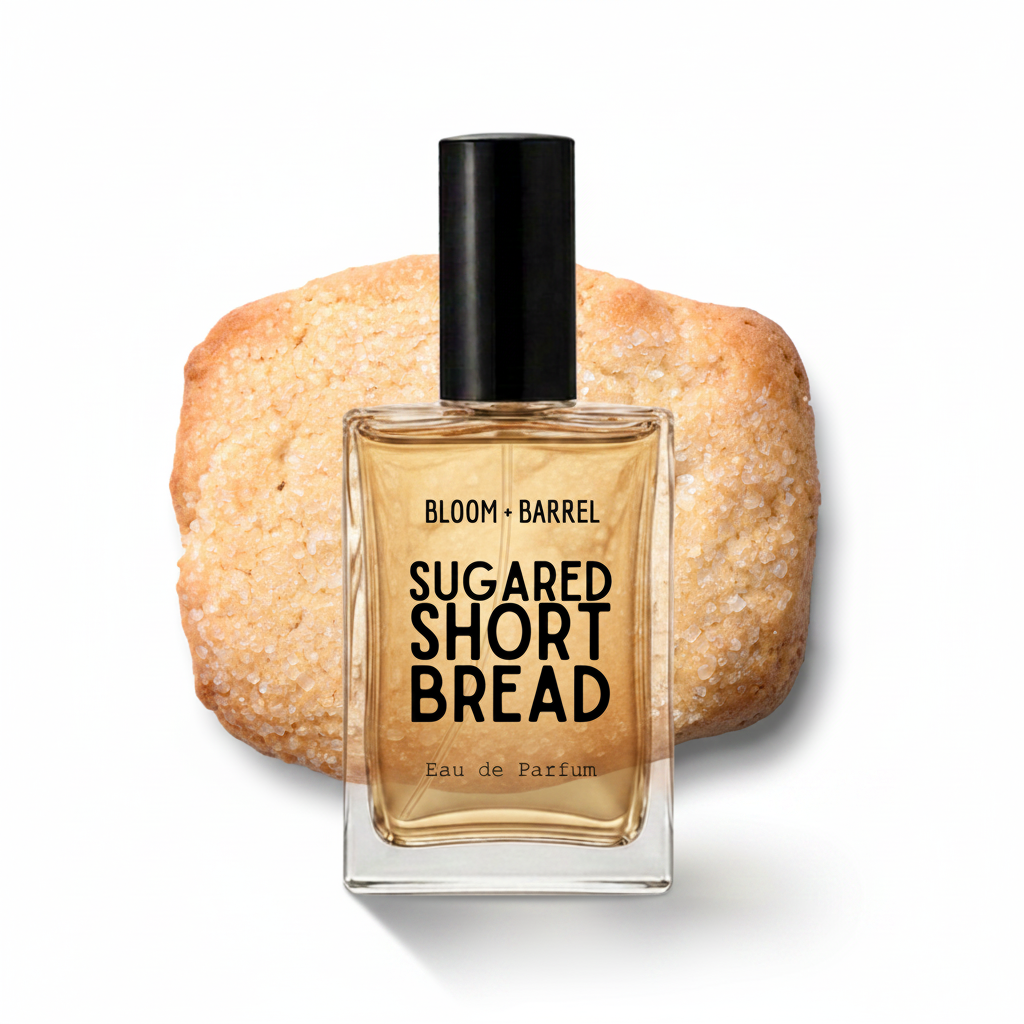 A square glass perfume bottle labeled 'BLOOM • BARREL SUGARED SHORT BREAD Eau de Parfum' with a black cap, set in front of a sugar-dusted shortbread cookie on a white background.