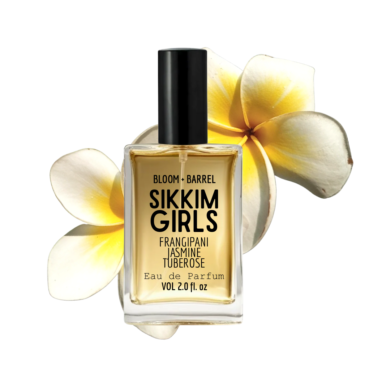 A rectangular glass perfume bottle with a black cap, labeled 'BLOOM + BARREL SIKKIM GIRLS', filled with golden-yellow fragrance. The bottle is centered against a white background with two large pale yellow and cream plumeria flowers behind it.