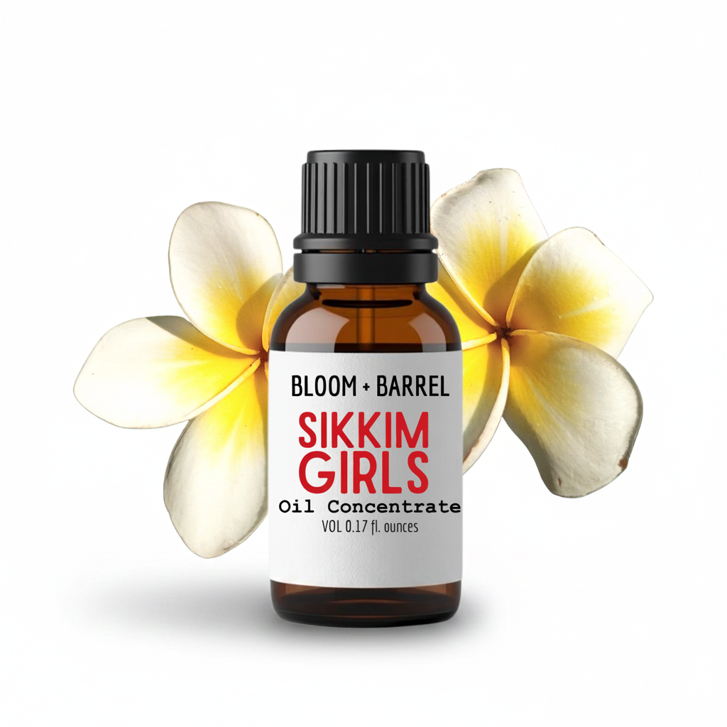A small amber glass bottle labeled 'BLOOM + BARREL SIKKIM GIRLS Oil Concentrate' with a black cap, centered on a white background and framed by two yellow-and-white plumeria flowers behind it.