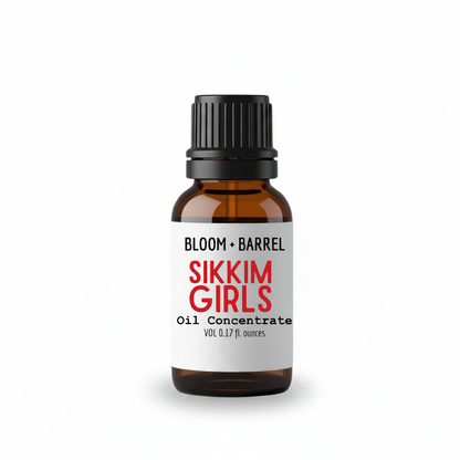 A small amber glass bottle with a black ribbed cap and a white label reading 'BLOOM + BARREL' and 'SIKKIM GIRLS Oil Concentrate' on a plain white background.