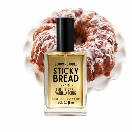 Bloom + Barrel Sticky Bread Eau de Parfum bottle in front of a glazed cinnamon coffee cake on a white plate, against a white background.