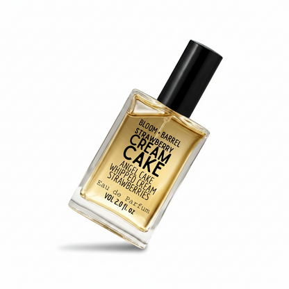 A rectangular glass bottle of Bloom + Barrel Strawberry cream cake Eau de Parfum with a black cap, filled with golden-amber liquid, on a plain white background.