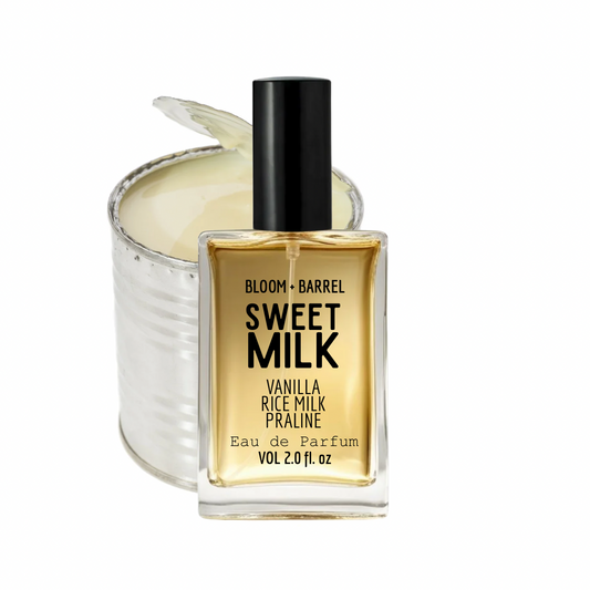 Bloom + Barrel Sweet Milk Eau de Parfum bottle in front of a silver tin candle with a wick, on a white background.