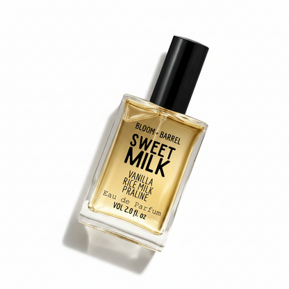 A rectangular glass bottle of Bloom + Barrel Sweet Milk Eau de Parfum with a black cap, filled with golden-amber liquid, on a plain white background.