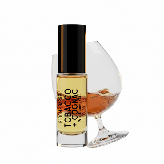 Bottle of Bloom Tobacco Barrel Cognac perfume next to a glass of cognac on a white background