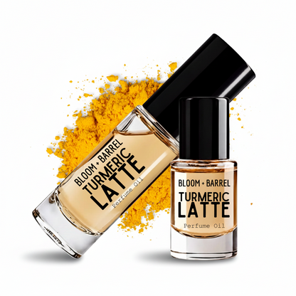 Two bottles of Bloom + Barrel Turmeric Latte perfume oil on a white background, one bottle lying diagonally with a yellow powder spill behind it and the other standing upright. The oil is a warm golden yellow color.