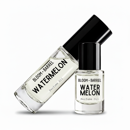 Two clear glass perfume oil bottles with black caps on a white background. One bottle is tilted diagonally and reads 'BLOOM + BARREL WATERMELON Perfume Oil,' while the other stands upright with the same label.
