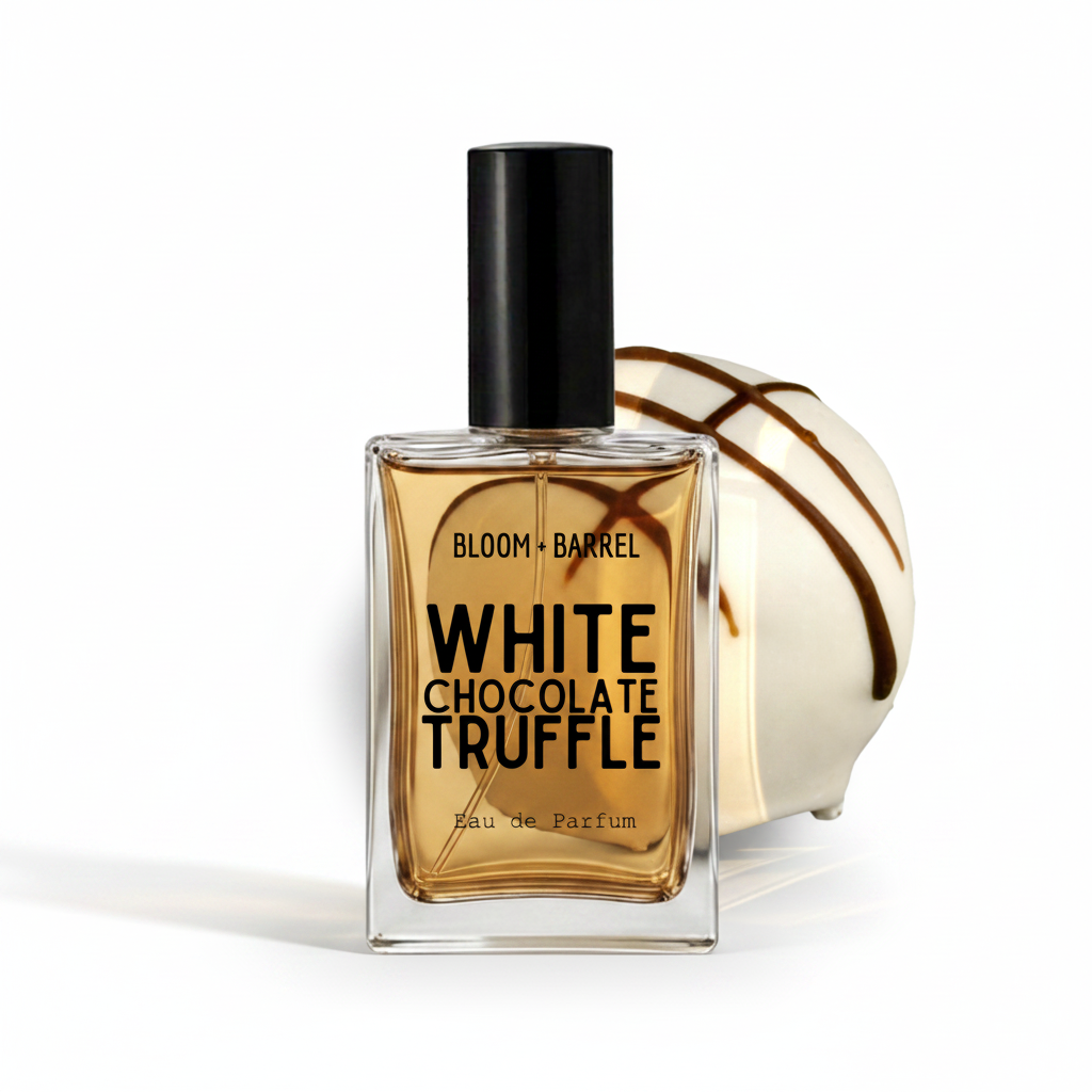 A rectangular glass perfume bottle with a black cap, filled with amber liquid, labeled 'BLOOM • BARREL WHITE CHOCOLATE TRUFFLE Eau de Parfum.' A white chocolate truffle with dark drizzle sits behind the bottle on a clean white background.