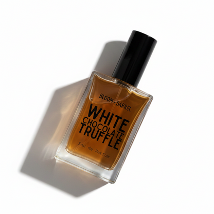 A rectangular glass perfume bottle filled with amber-brown liquid, featuring a black cylindrical cap and a clear label with bold black text reading 'BLOOM • BARREL' and 'WHITE CHOCOLATE TRUFFLE' on a plain white background.