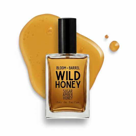 A bottle of Bloom + Barrel Wild Honey Sugar Amber Eau de Parfum centered in front of a glossy smear of honey on a white background.