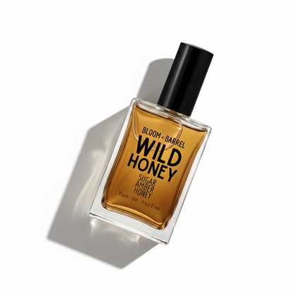 A rectangular glass bottle of Wild Honey Eau de Parfum by Bloom Barrel, filled with amber-colored liquid and featuring a black cap, set against a plain white background.
