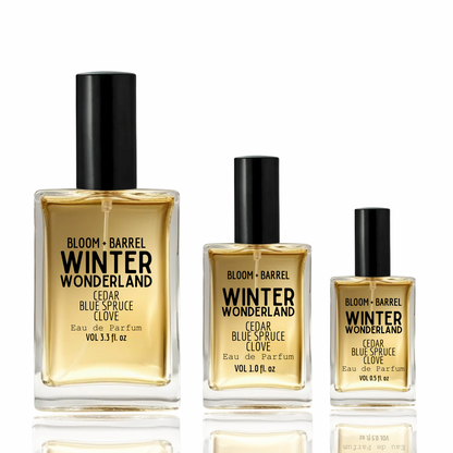Three Bloom Barrel Winter Wonderland Eau de Parfum bottles in different sizes with black caps, filled with amber-colored liquid, on a white background with reflections.