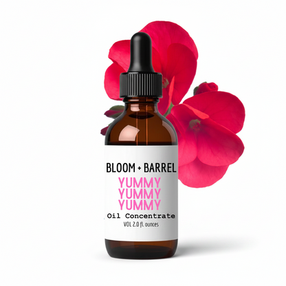 Bottle of Bloom + Barrel Yummy Yummy Oil Concentrate with red flowers in the background